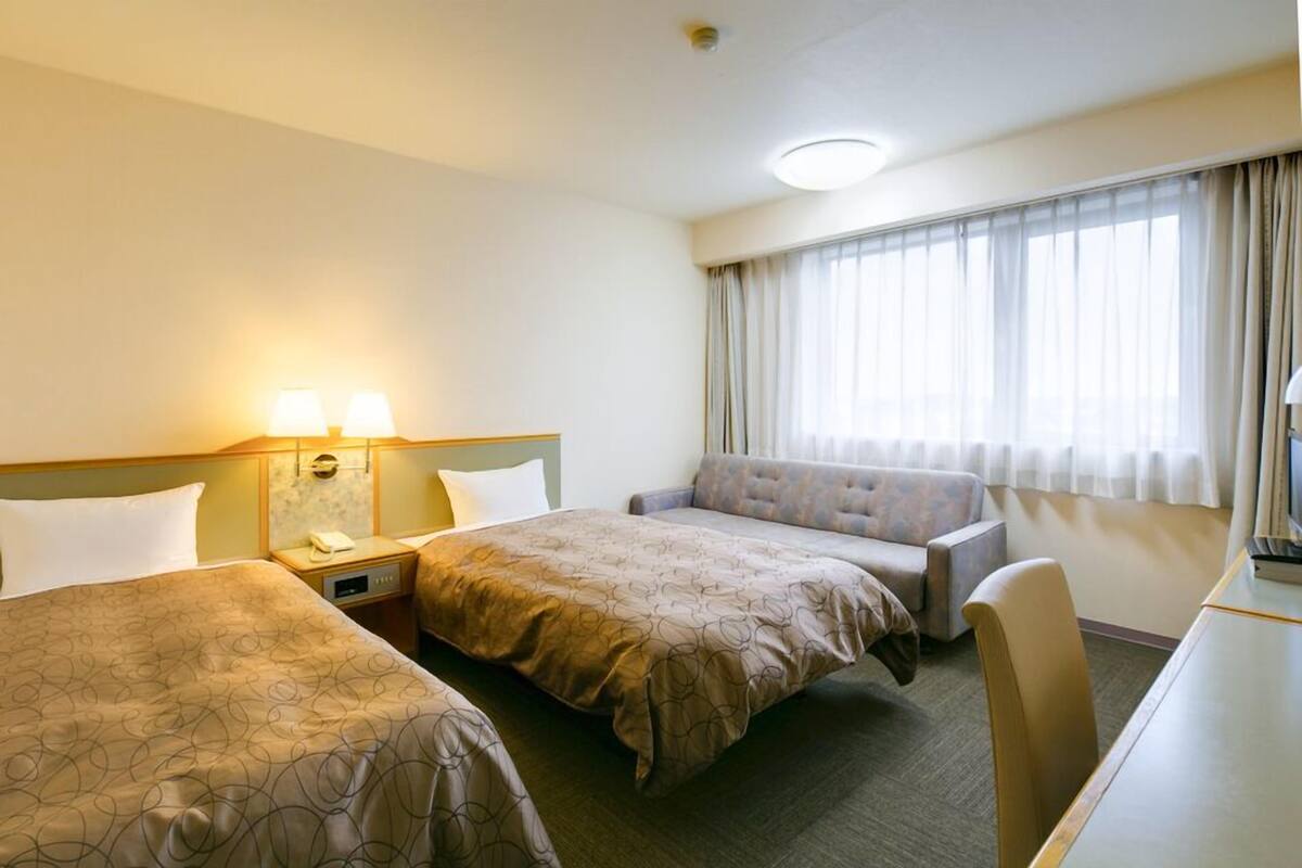 Habitación de hotel con dos camas, un sofá, un escritorio y una ventana con cortinas.