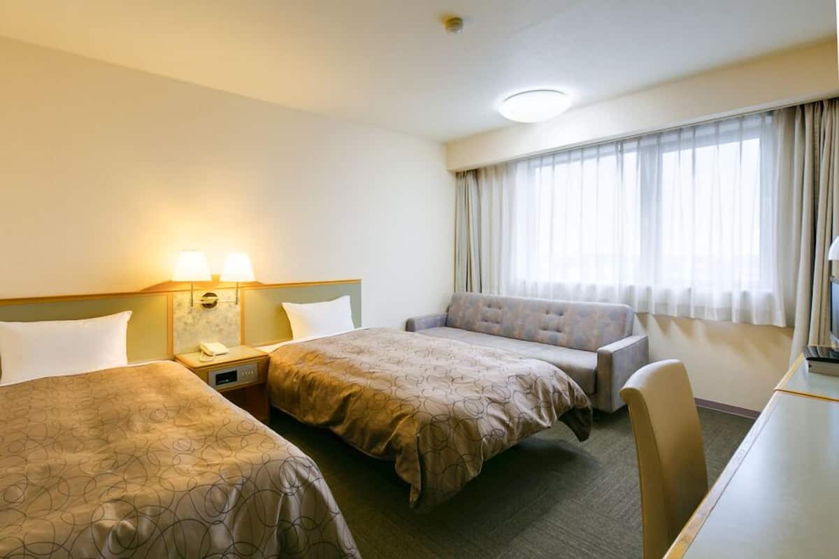 A hotel room with two beds, a sofa, a desk, and a window with curtains.