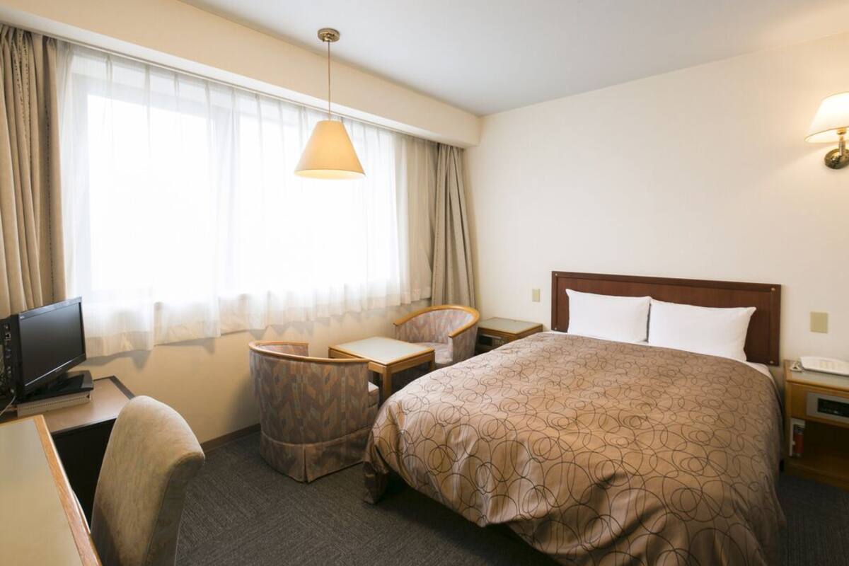 Habitación de hotel con cama, escritorio, silla y televisor.