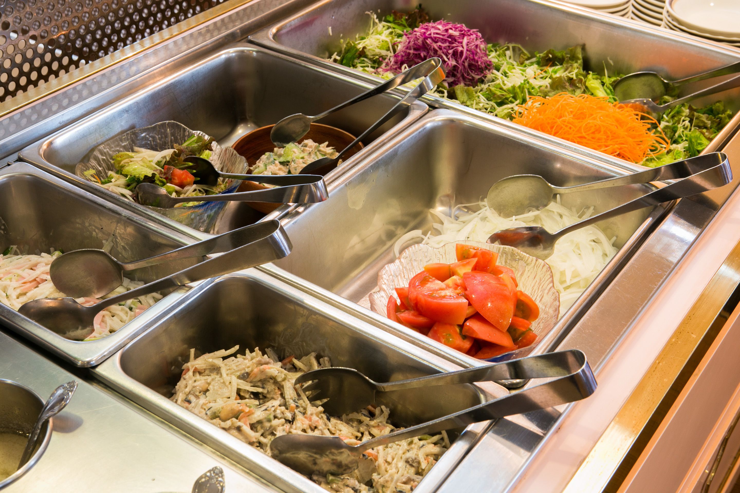 En buffet med forskellige madmuligheder, herunder salater, revne grøntsager og en fiskeret.