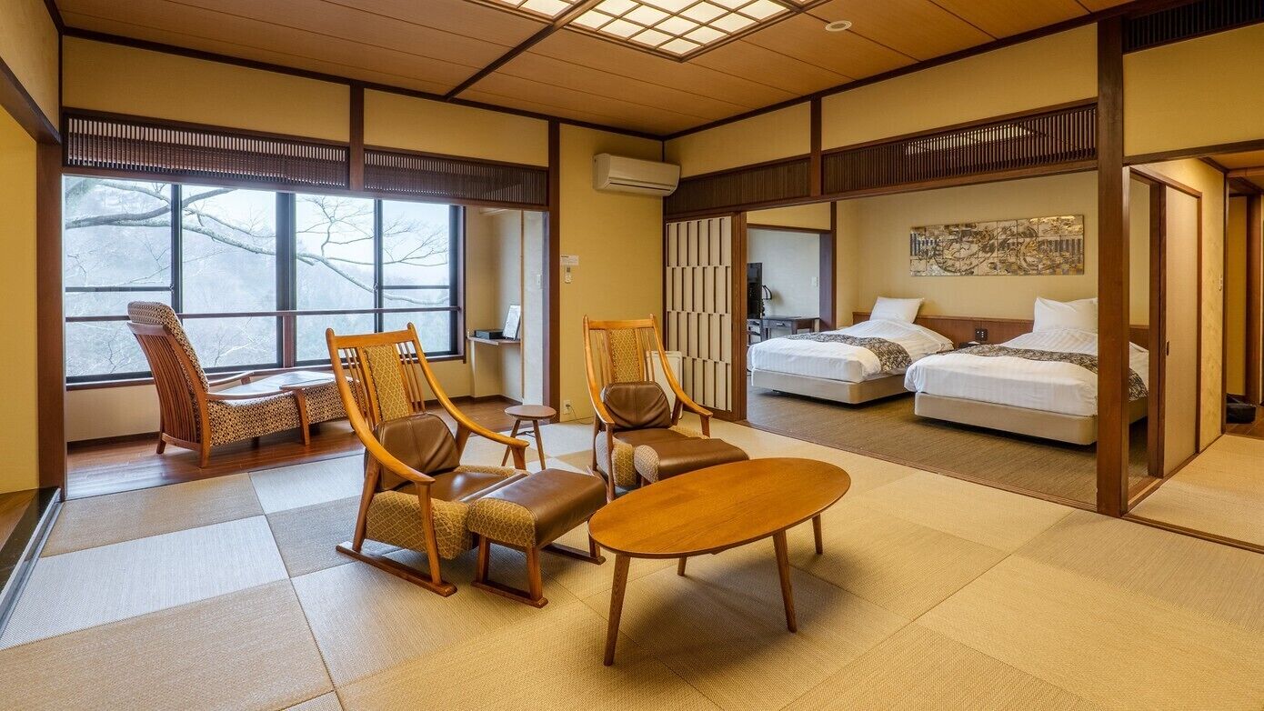 A traditional Japanese-style room with tatami flooring, a sofa, two chairs, a small table, and a bed with a futon.