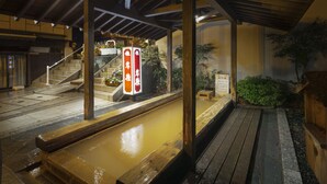 A traditional Japanese onsen with wooden structures and a stone pathway leading to a hot spring area. - Kishigon Ryokan (Shibukawa)