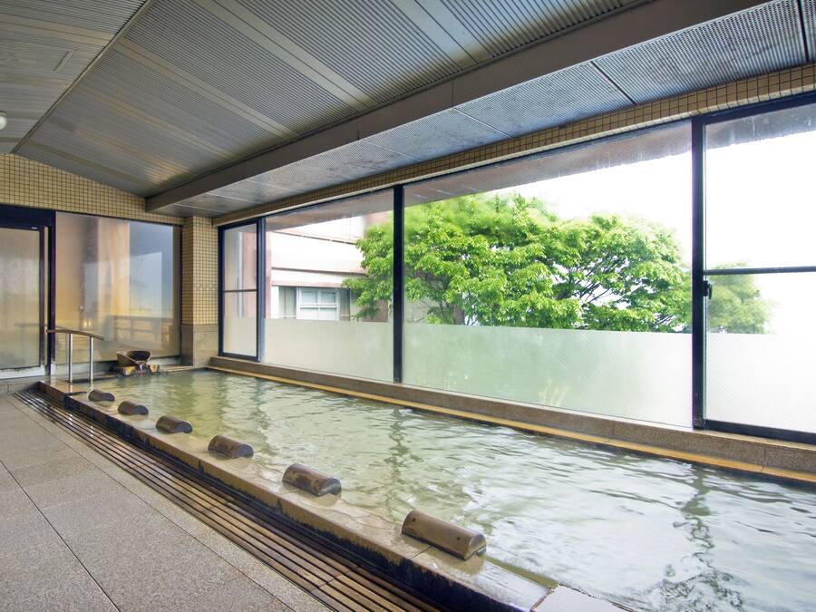 A large indoor pool with clear glass walls, a tiled floor, and a view of trees outside.