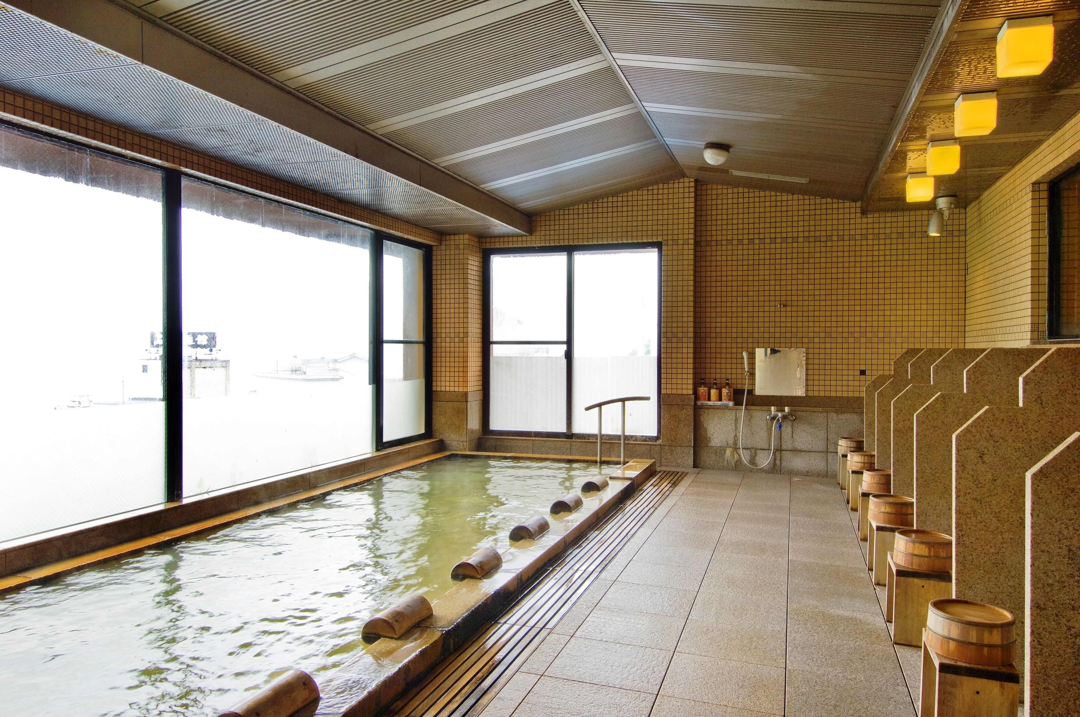 Un onsen japonés tradicional con una extensa fuente termal, bancos de madera y paredes de azulejos.