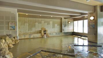 Una amplia piscina interior con paredes de azulejos y suelo de piedra. Se observan rocas a la izquierda y una pequeña cascada en el centro.