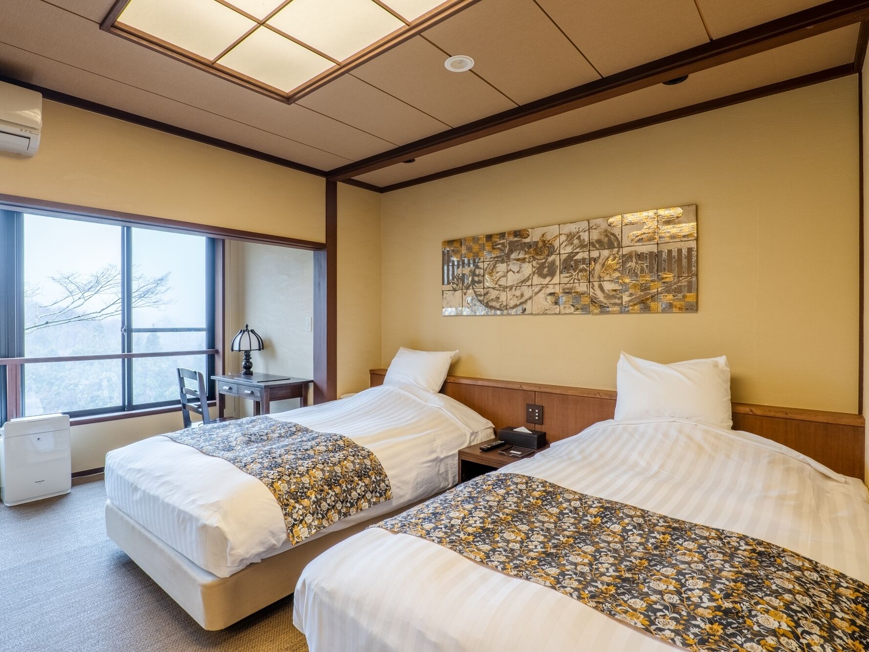 A hotel room with two beds, a desk, a chair, and a large window.