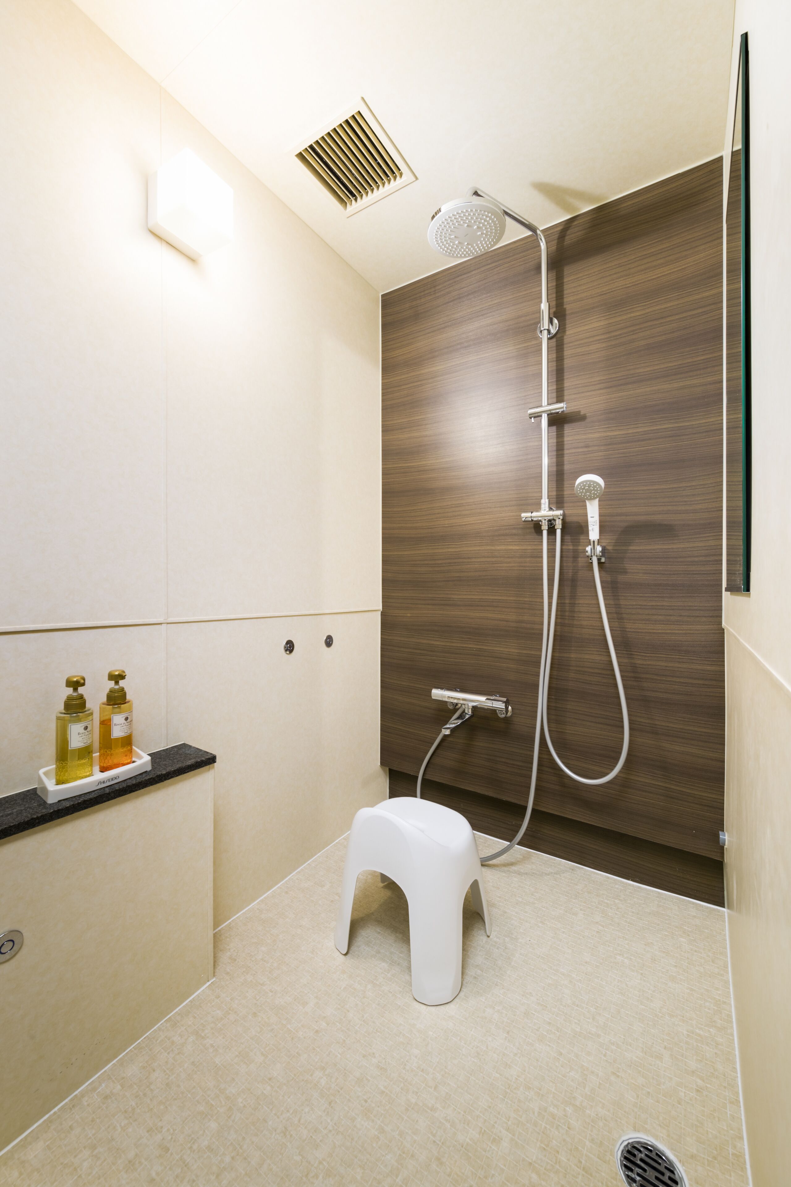 A modern bathroom with a shower, a small stool, and two bottles of soap on a counter.