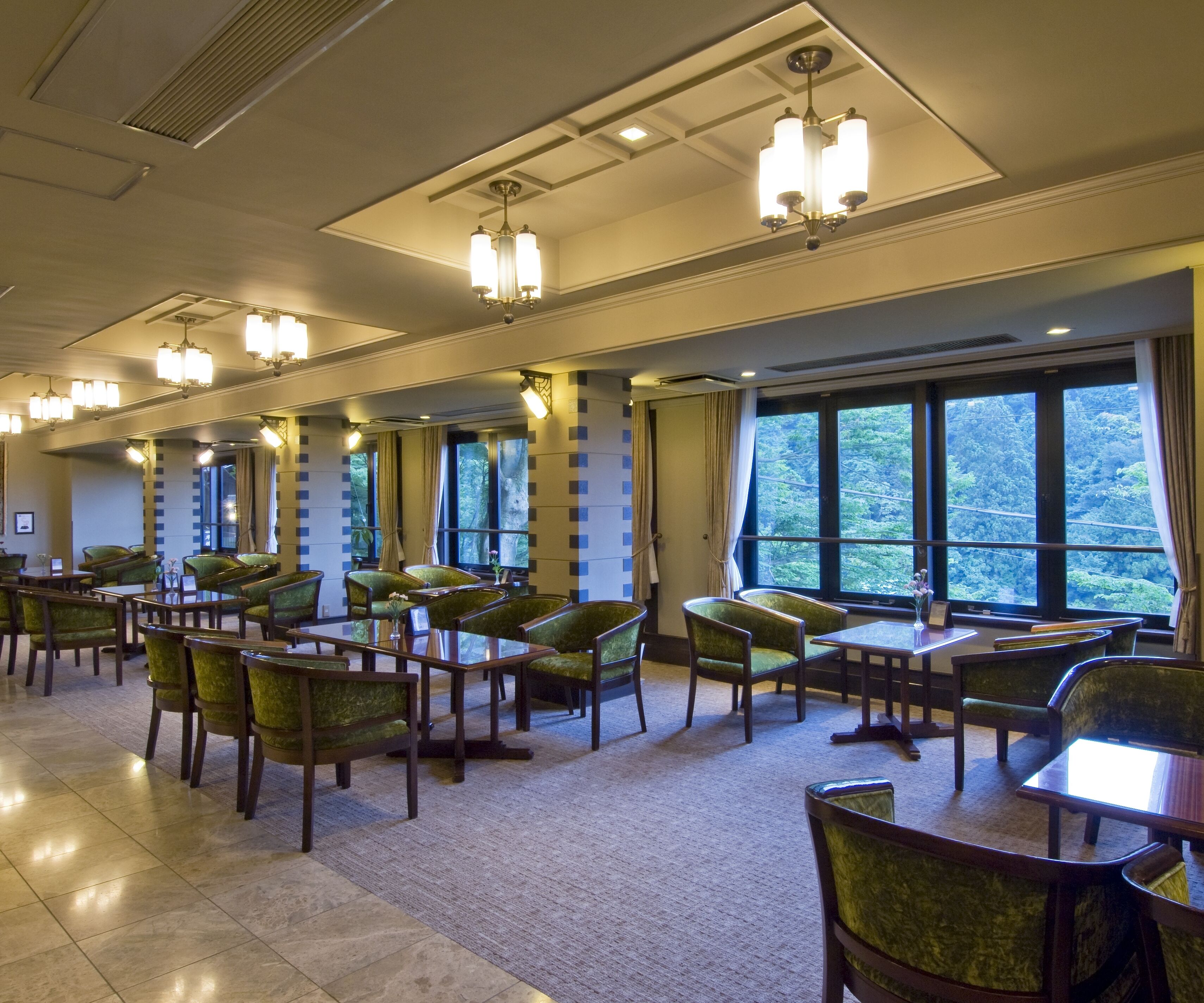 Un vaste espace dédié à la salle à manger, avec de nombreuses tables et chaises, de grandes fenêtres offrant une vue sur la forêt et un éclairage moderne.