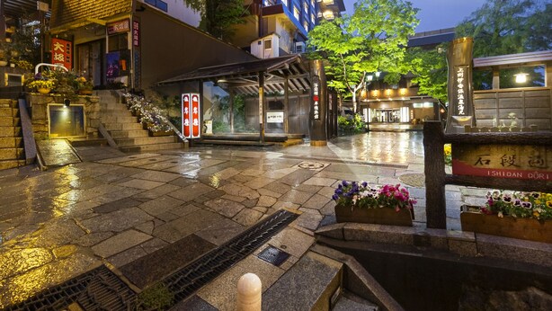 A traditional Japanese building with a stone staircase leading to the entrance, surrounded by greenery and illuminated by warm lighting. - Kishigon Ryokan (Shibukawa)
