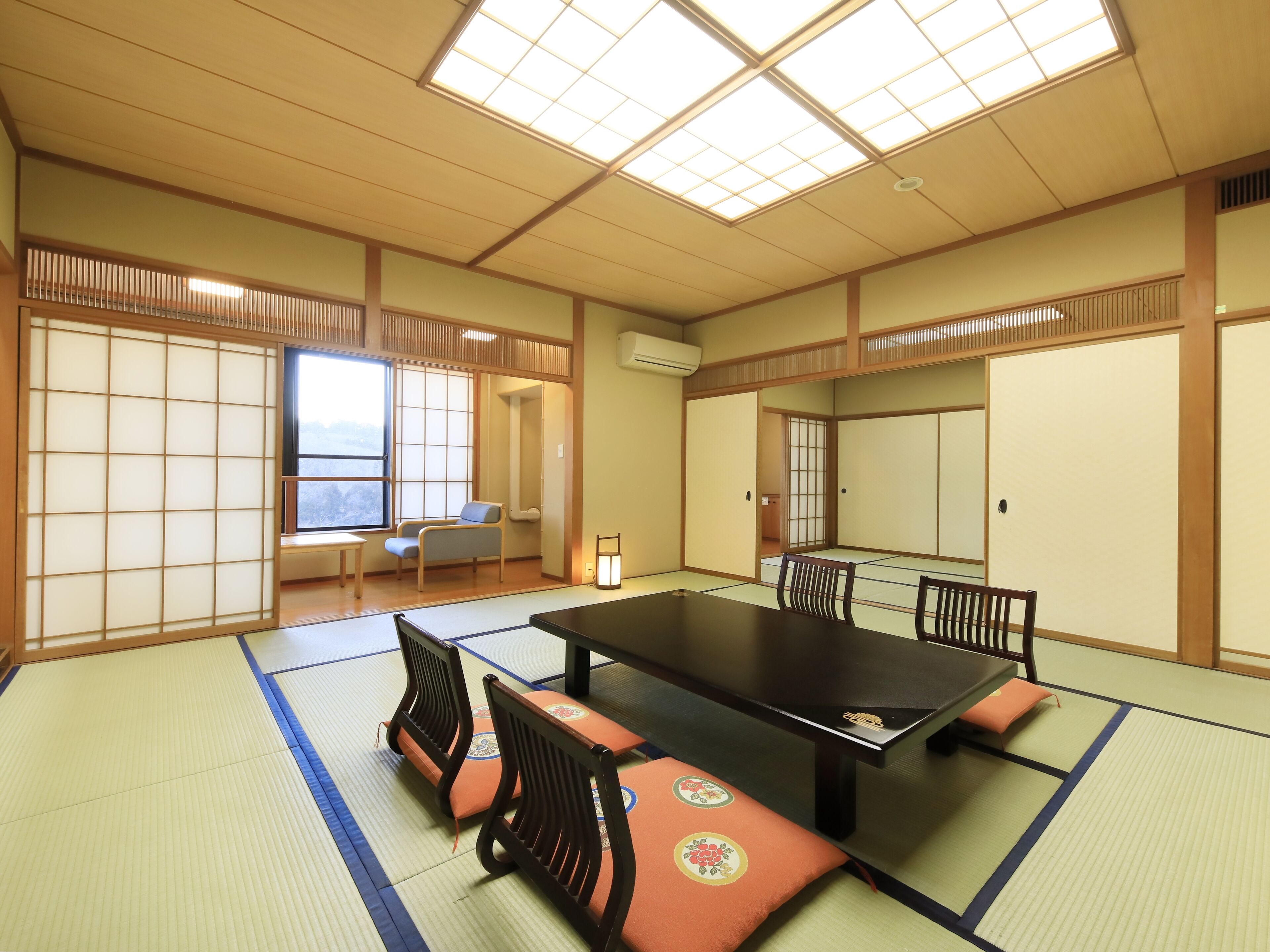 A tatami mat room with a low table and chairs, large windows, and sliding doors.