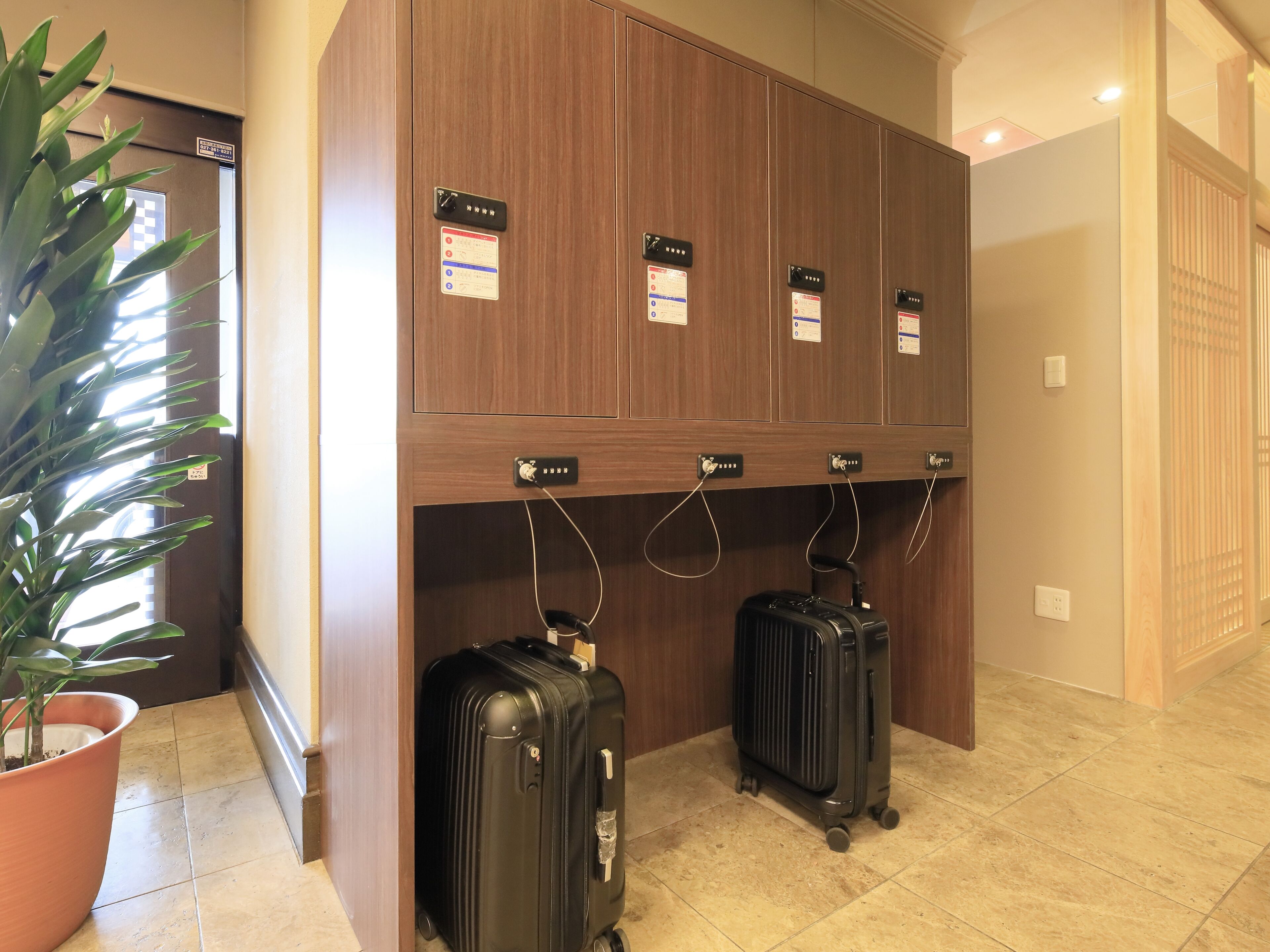 A hotel lobby with a wooden reception desk, multiple lockers, and two suitcases on the floor.