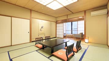 A traditional tatami mat room with a tatami mat table, wooden chairs, a sliding door, and a large window with a view.
