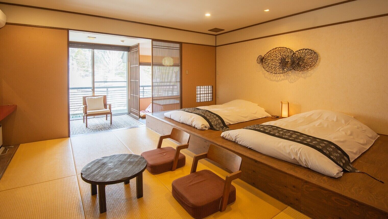 A room with two beds, a tatami mat floor, a small table, and a sliding door leading to an outdoor area.
