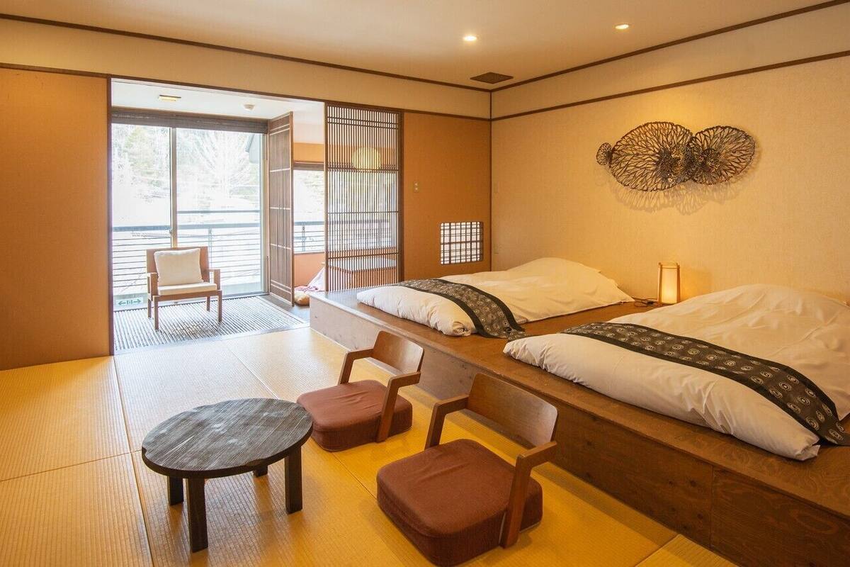 Una habitación con dos camas, suelo de estequilla, una mesita y una puerta corredera que da a un espacio exterior.