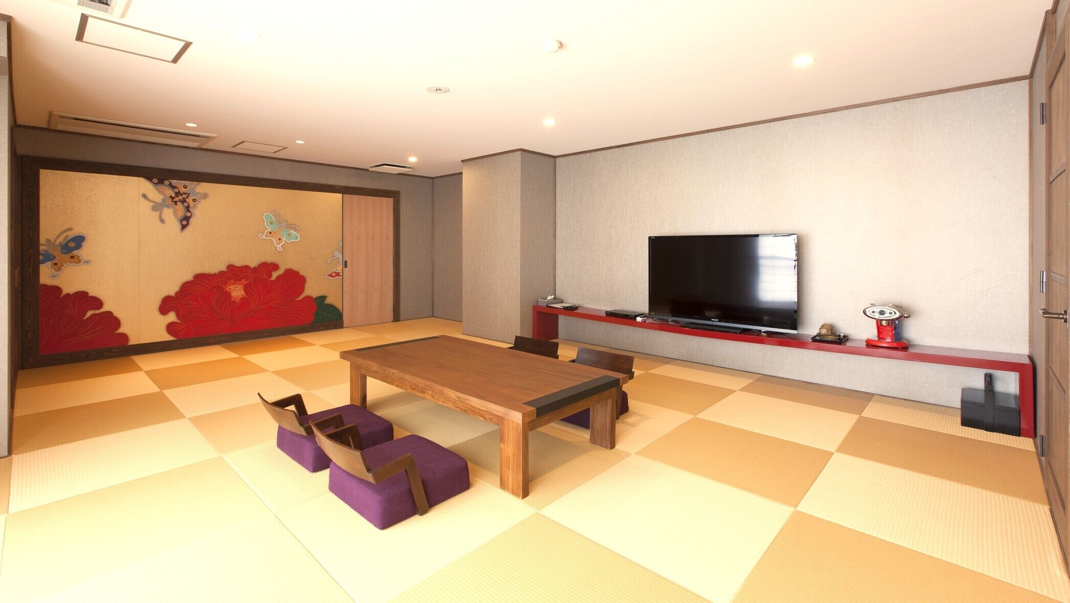 A room with tatami flooring, a wooden table, purple cushions, a flat-screen TV, and a red entertainment unit.