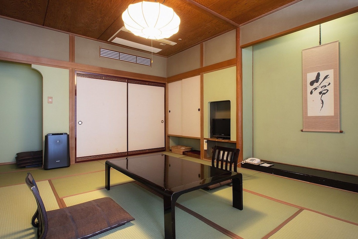 Une pièce de style japonais traditionnel, avec un sol recouvert de tatamis, une table basse, un téléviseur et des portes coulissantes.