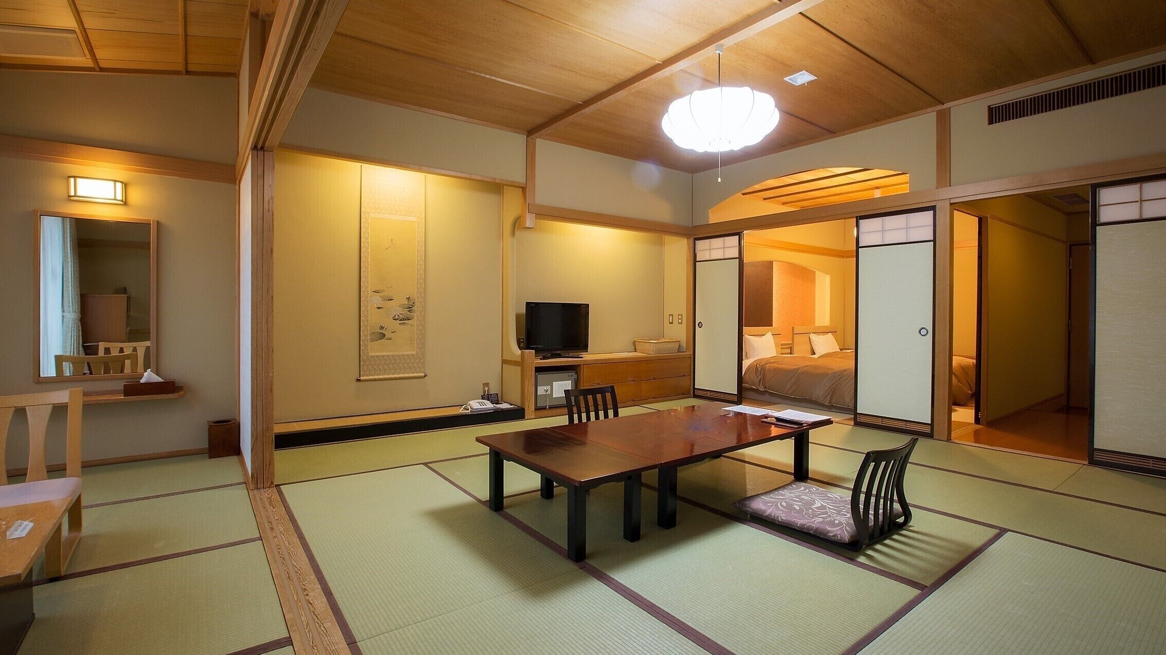 Une pièce de style japonais traditionnel, avec un sol recouvert de tatamis, une table basse, un téléviseur et des portes coulissantes.