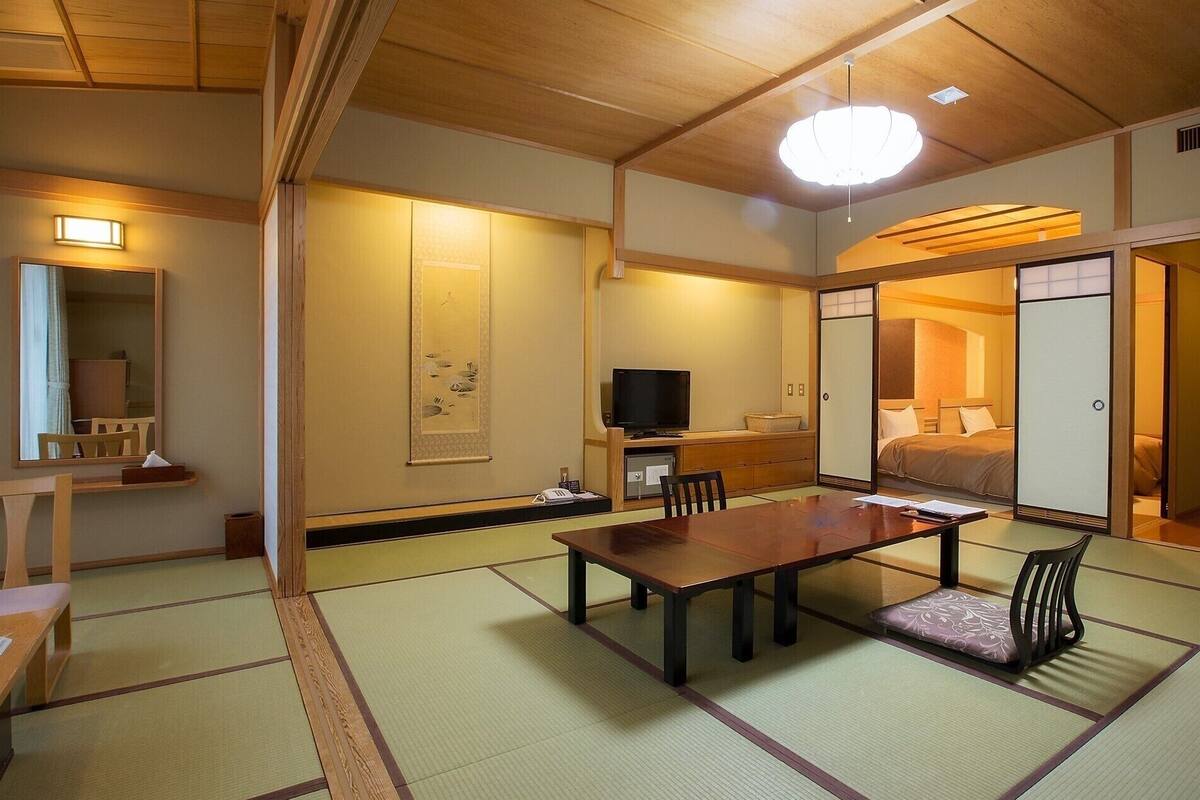 Une pièce de style japonais traditionnel, avec un sol recouvert de tatamis, une table basse, un téléviseur et des portes coulissantes.