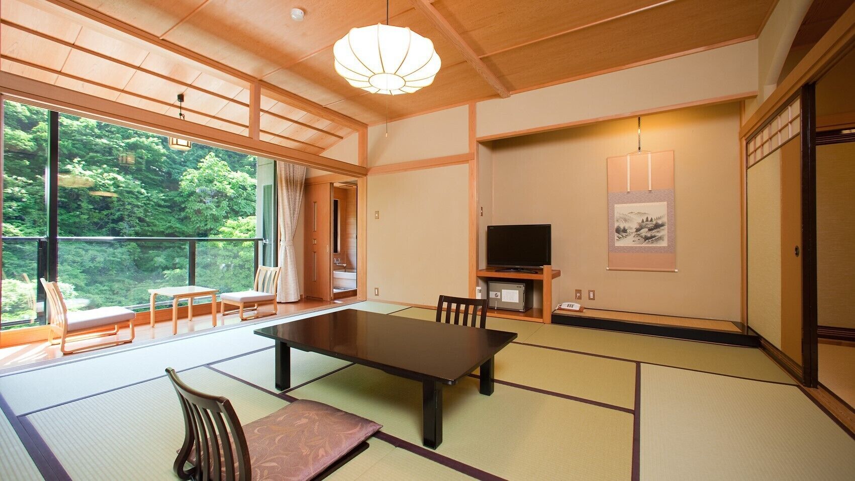 Une pièce de style japonais traditionnel, avec un sol recouvert de tatamis, une table basse, des chaises, un téléviseur et un tableau accroché au mur.