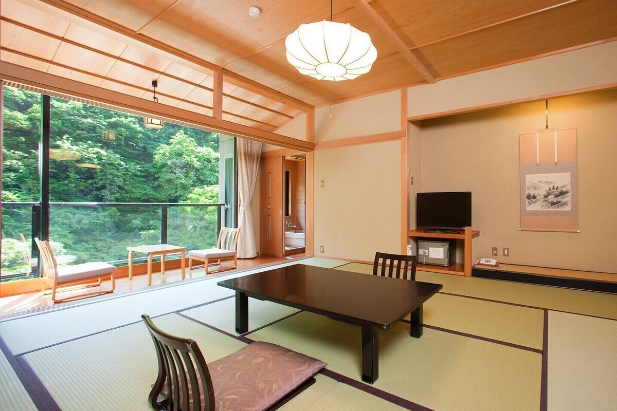 Une pièce de style japonais traditionnel, avec un sol recouvert de tatamis, une table basse, des chaises, un téléviseur et un tableau accroché au mur.