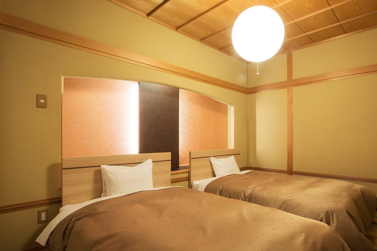 Une chambre d’hôtel avec deux lits, des têtes de lit en bois, un grand miroir et un luminaire suspendu.