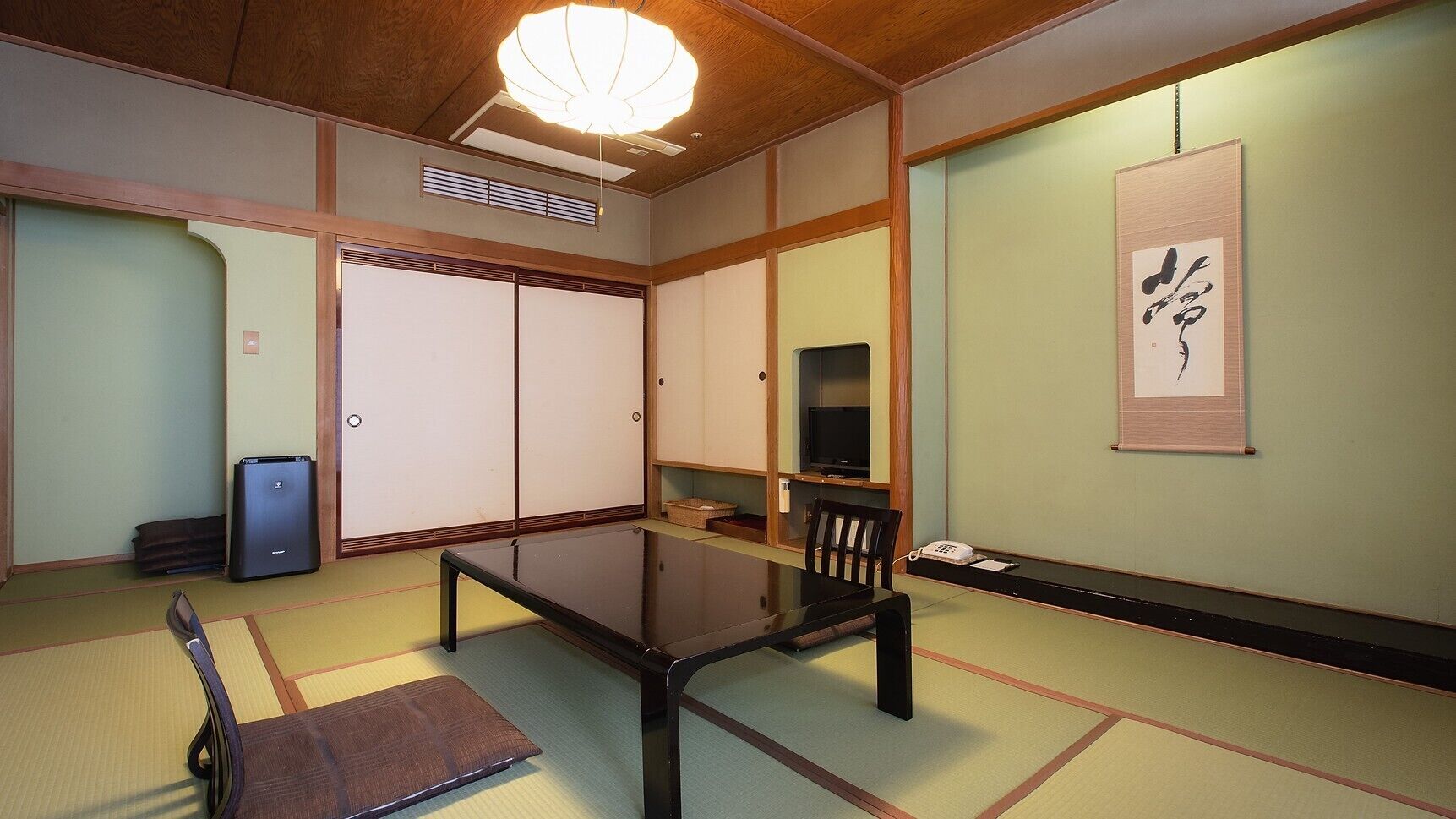 Une pièce de style japonais traditionnel, avec un sol recouvert de tatamis, une table basse, un téléviseur et des portes coulissantes.