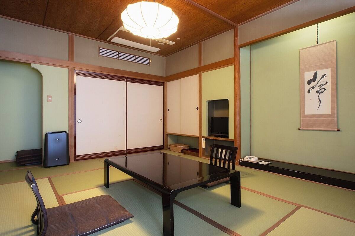 Une pièce de style japonais traditionnel, avec un sol recouvert de tatamis, une table basse, un téléviseur et des portes coulissantes.