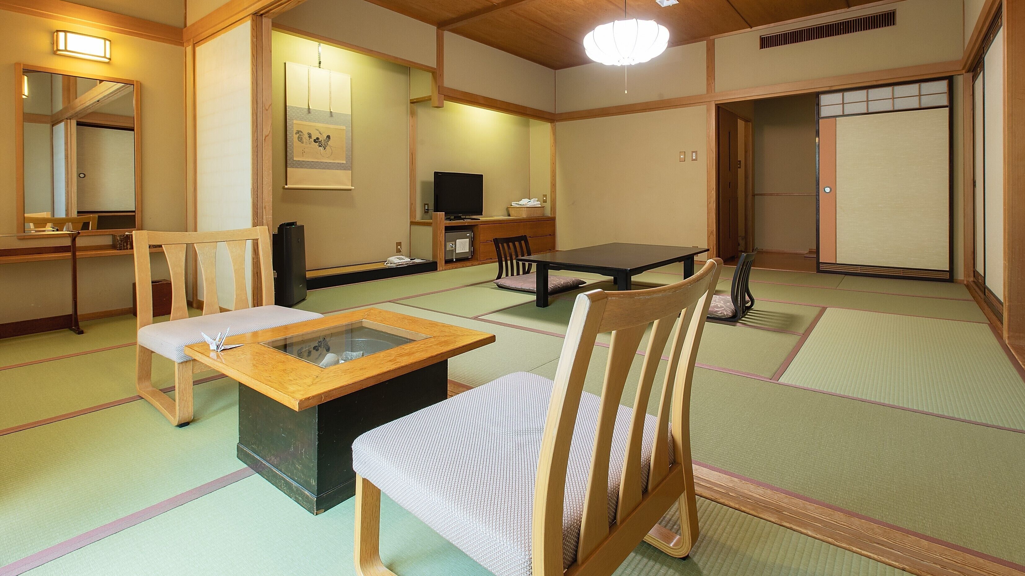 Une pièce de style japonais traditionnel, avec un sol recouvert de tatamis, une table basse, des chaises, un téléviseur et une porte coulissante.