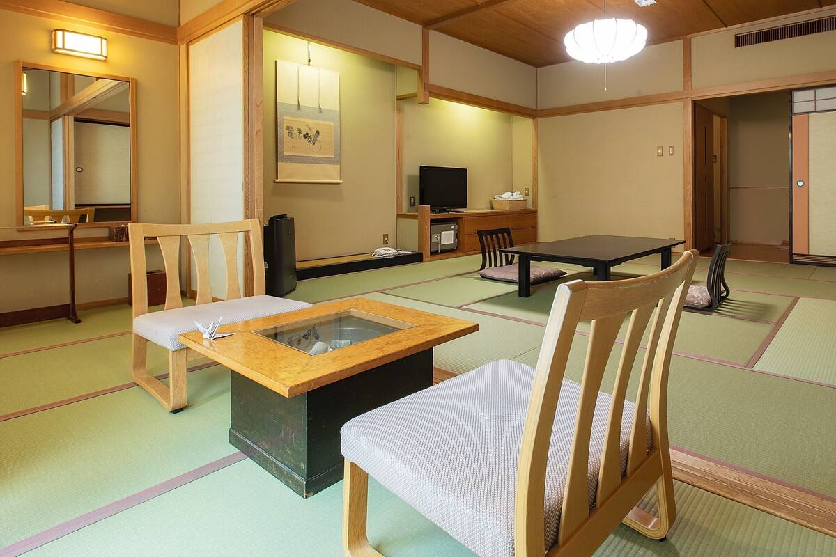 Une pièce de style japonais traditionnel, avec un sol recouvert de tatamis, une table basse, des chaises, un téléviseur et une porte coulissante.