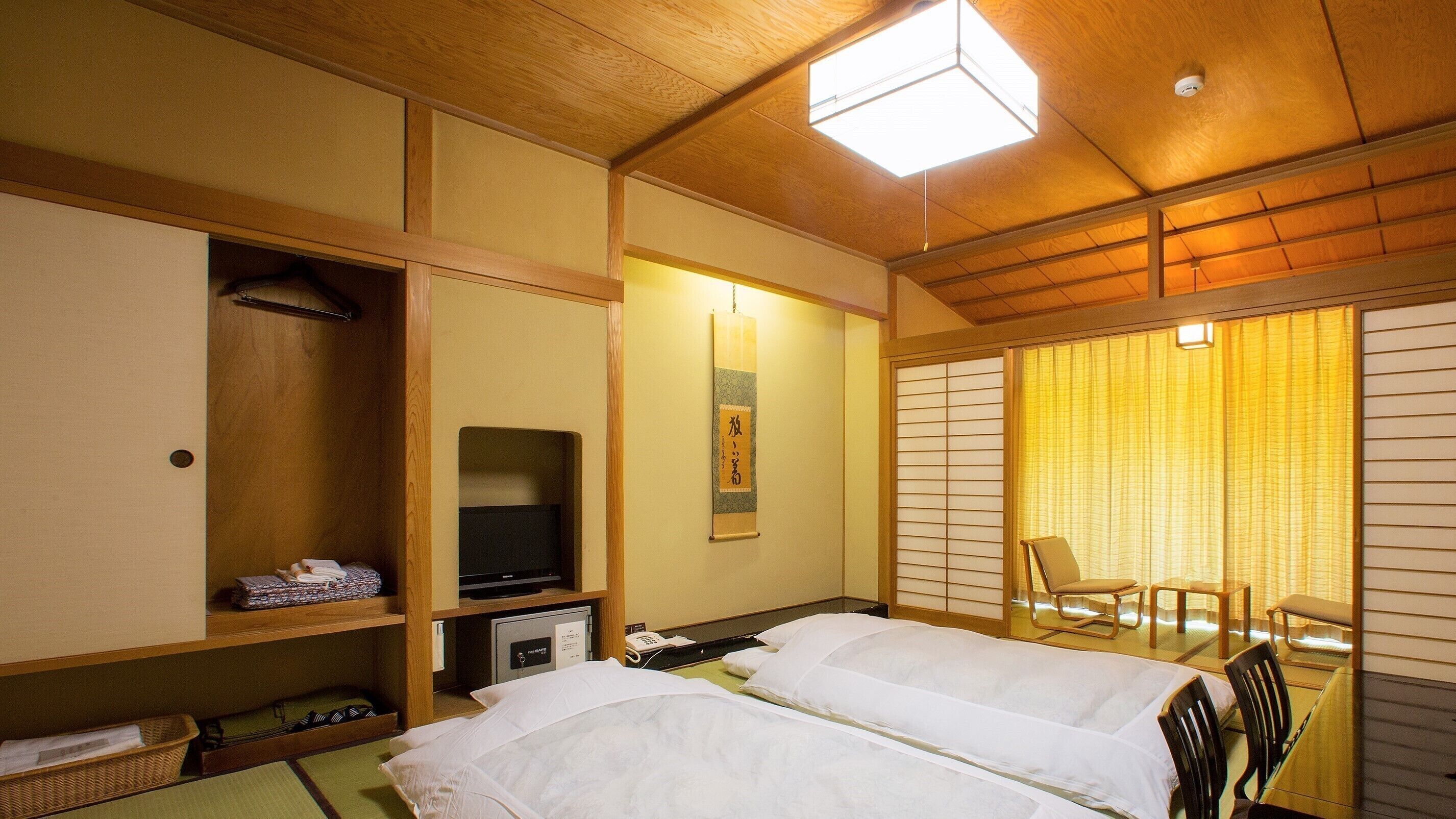 Une chambre d’hôtel avec deux lits, une télévision, une étagère avec des vêtements pliés, un bureau avec un téléphone et une porte coulissante donnant sur un balcon.
