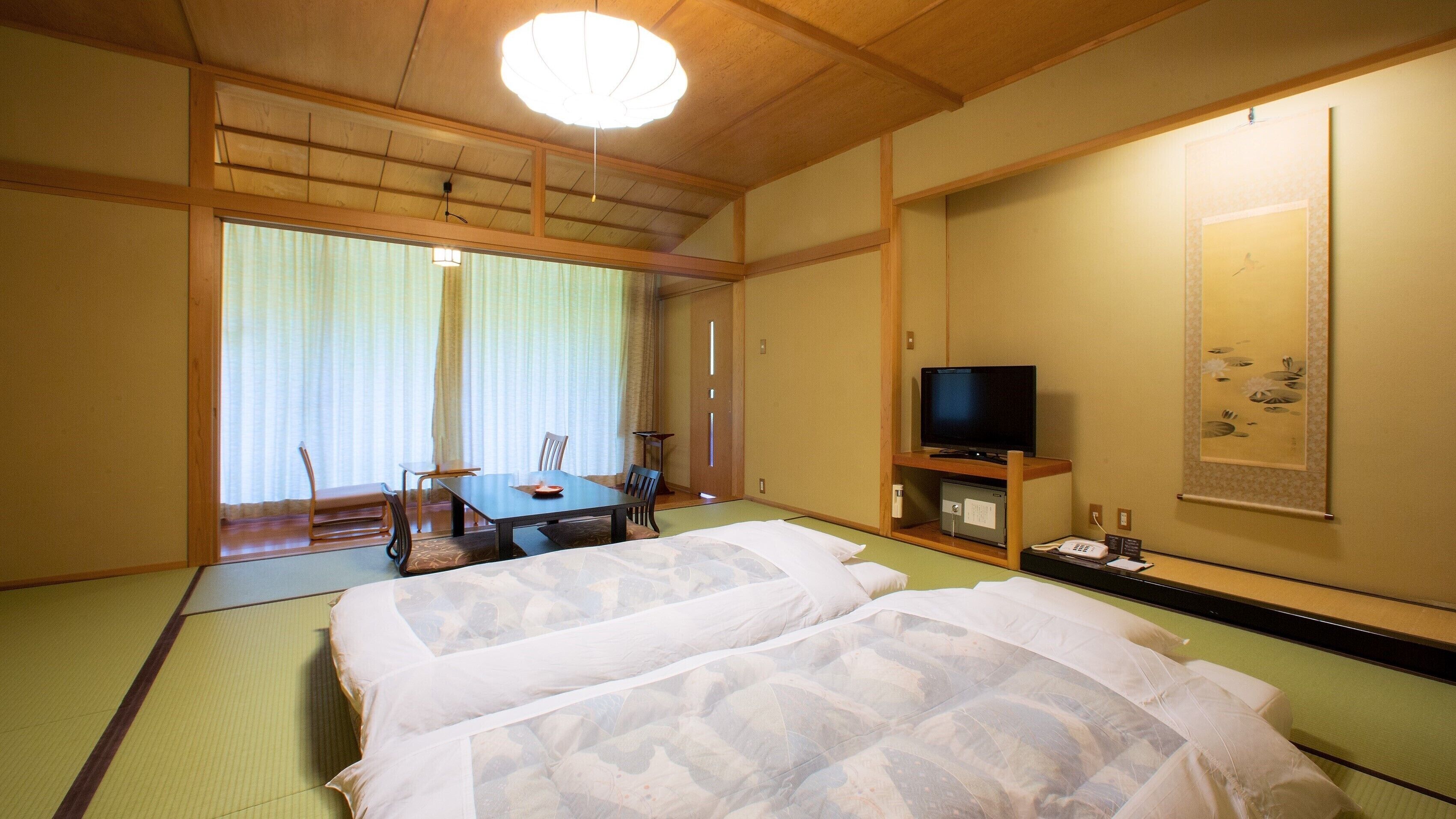 Une pièce de style japonais traditionnel, avec un sol recouvert de tatamis, un futon servant de lit, une télévision et une table à manger avec des chaises.