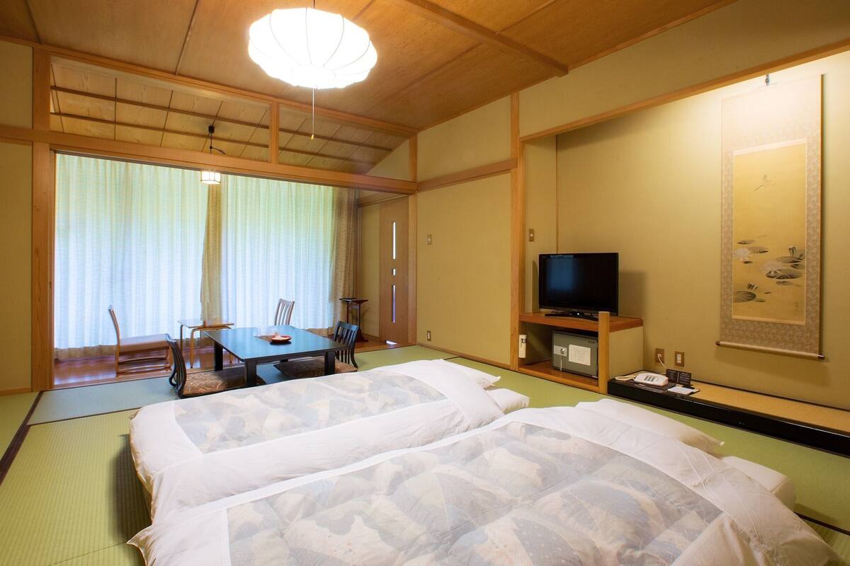 Une pièce de style japonais traditionnel, avec un sol recouvert de tatamis, un futon servant de lit, une télévision et une table à manger avec des chaises.