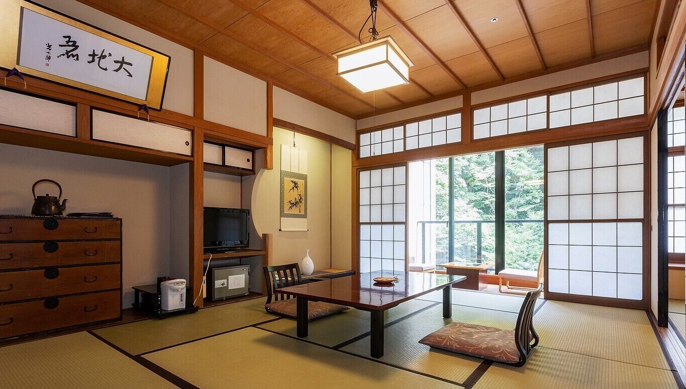 Une pièce de style japonais traditionnel, avec un sol recouvert de tatamis, une table basse, un téléviseur et une porte coulissante.