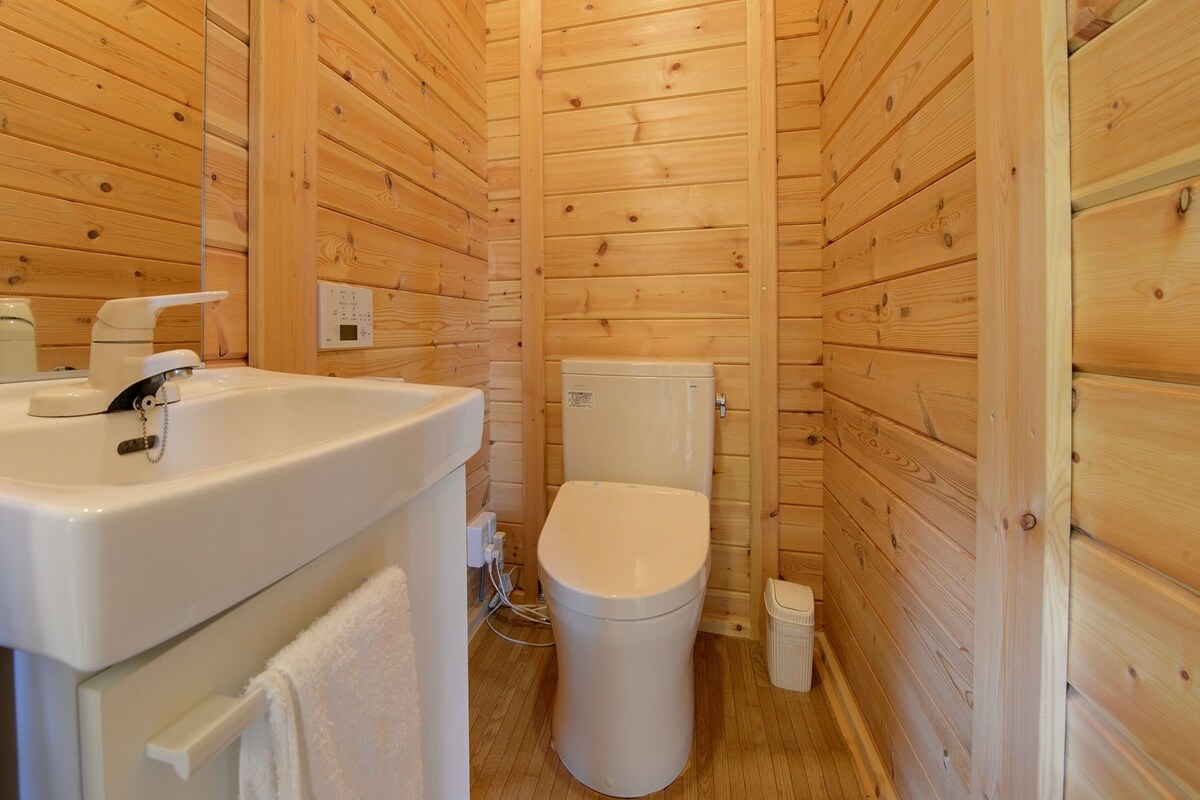 A compact wooden cabin bathroom with a sink, toilet, and a small trash bin.