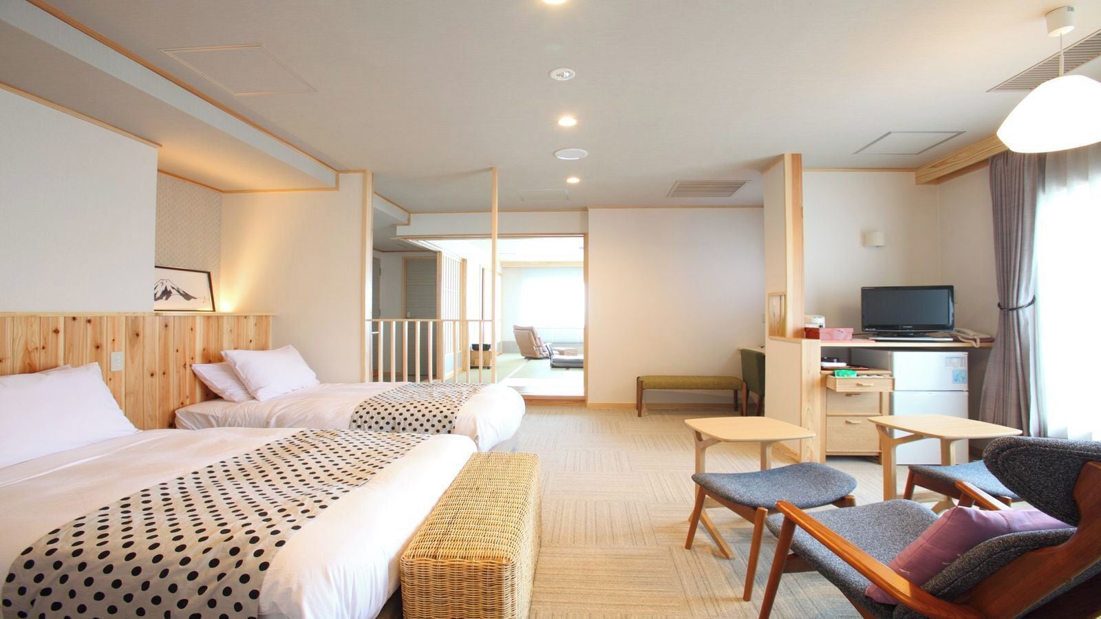 A hotel room with two beds, a desk, a television, and a seating area.