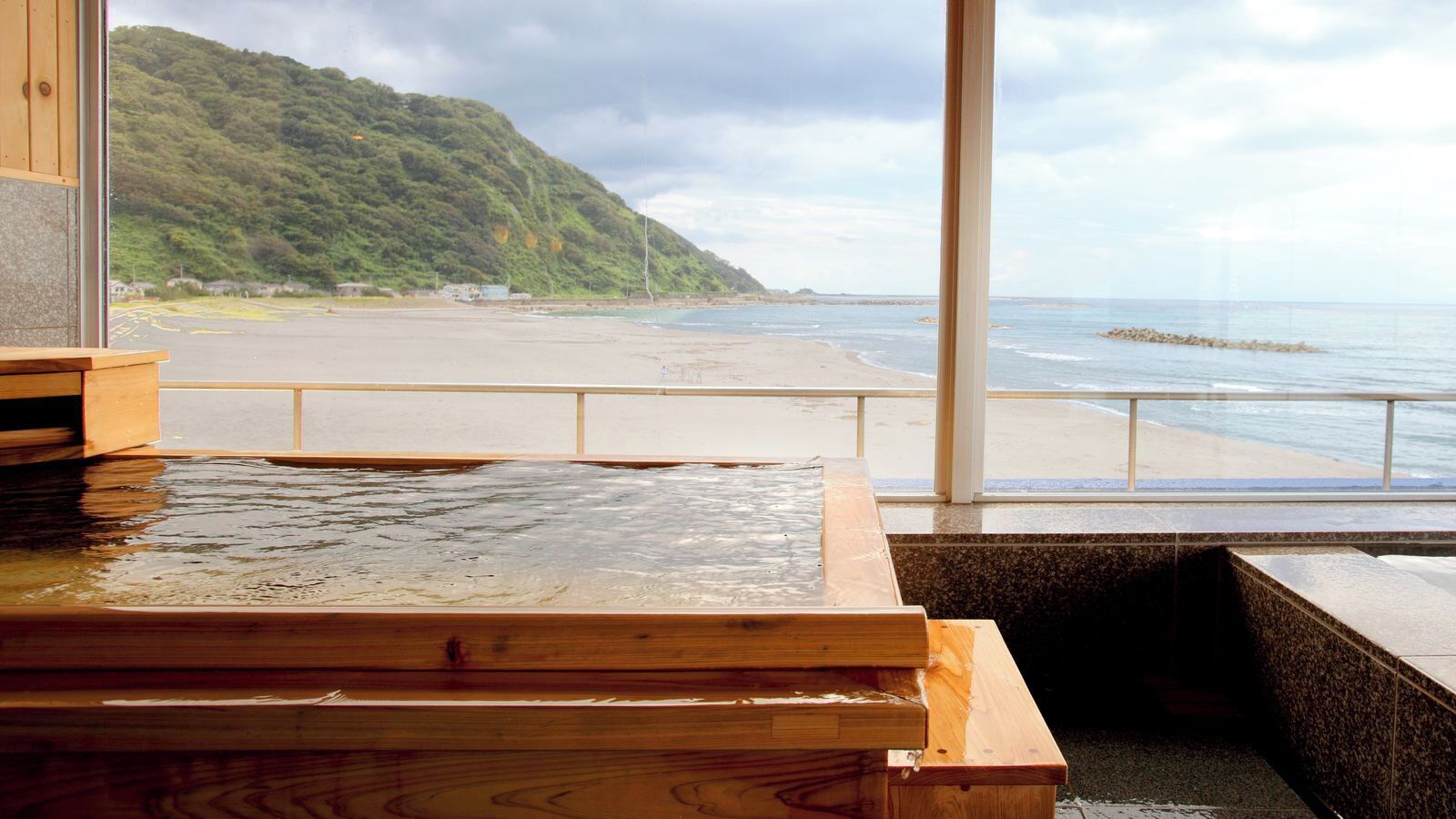 A wooden bath area with a view of a beach and a hill.