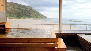 A wooden bath area with a view of a beach and a hill.