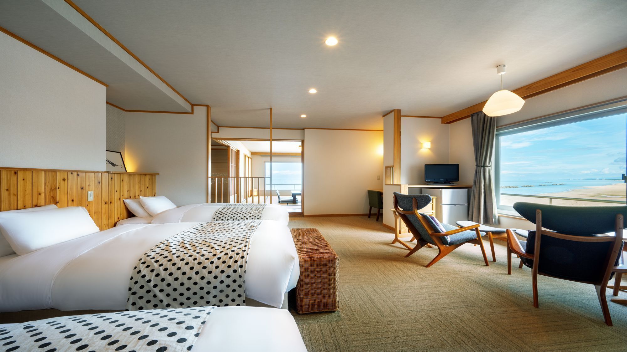 Una habitación de hotel con cama, escritorio con televisor, silla y vista a la playa.