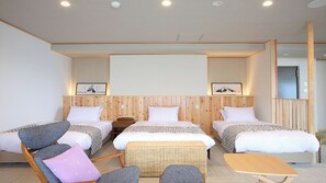 A hotel room with three beds, a wooden headboard, a small table, and two chairs.