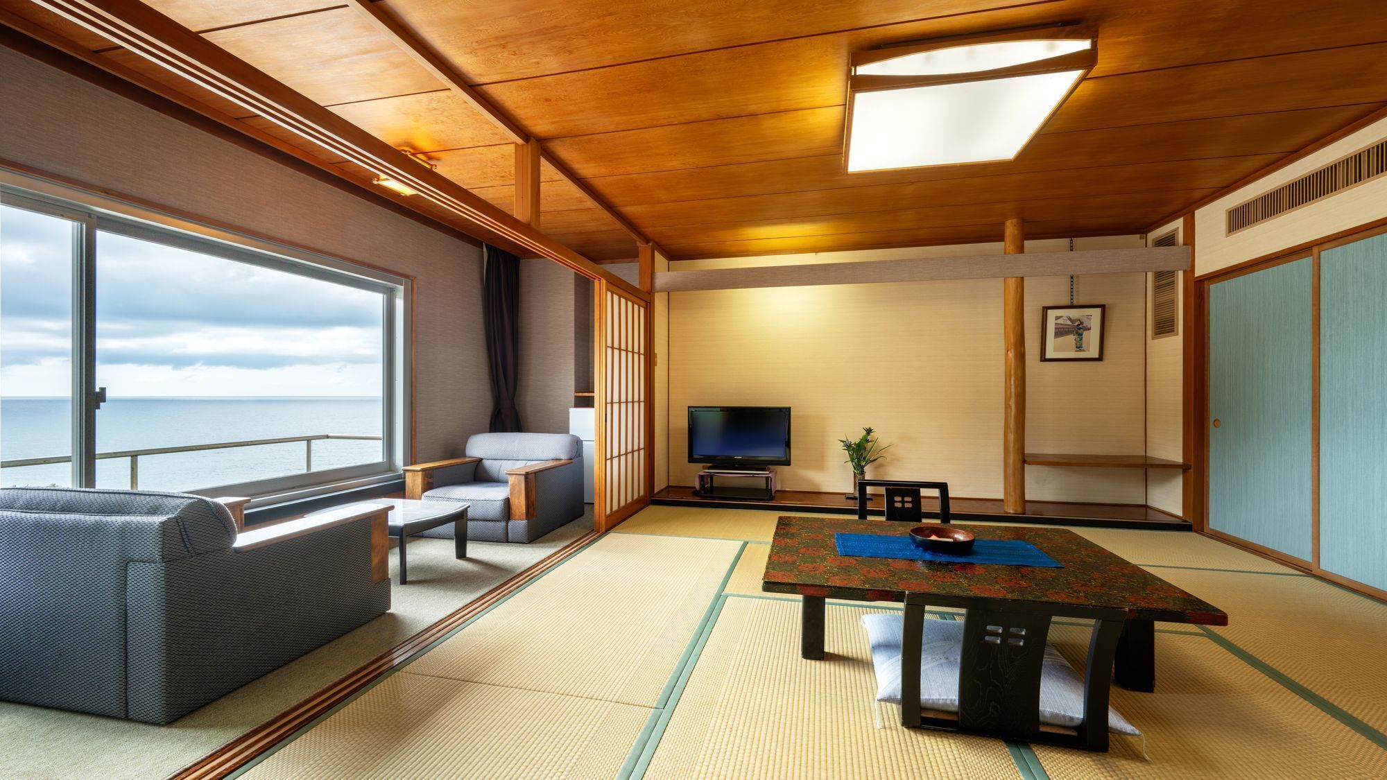 Una habitación con un ventanal grande, un sofá, un televisor, una mesa y esteras de tatami.