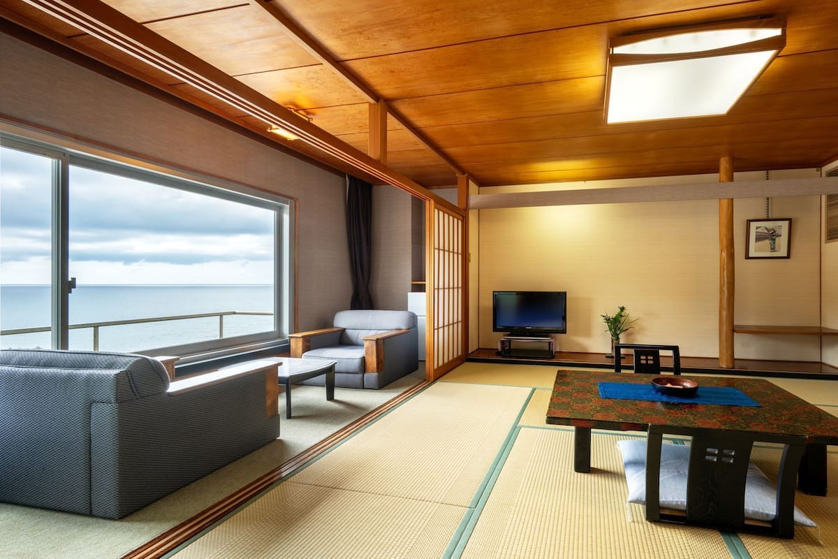 A room with a large window, a sofa, a TV, a table, and tatami mats.