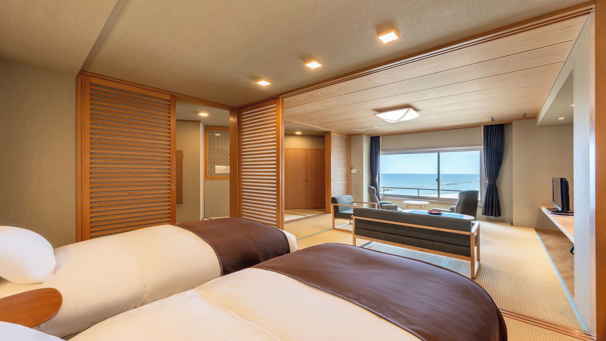 Habitación de hotel con dos camas, un escritorio con silla, una mesita y vista al mar.