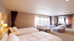 Quarto de hotel com duas camas, uma escrivaninha, uma cadeira e vista para o mar.