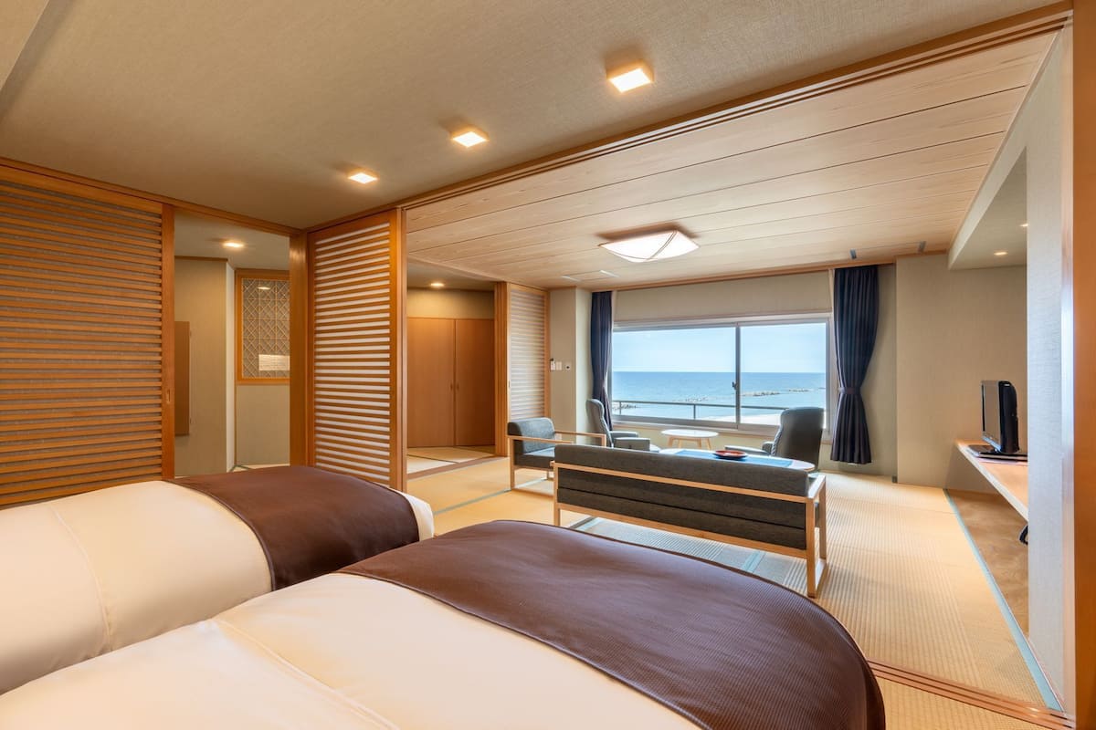 A hotel room with a bed, a desk, a chair, and a view of the sea.