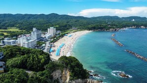 Un complejo turístico frente al mar, con playa, edificios y montañas al fondo.