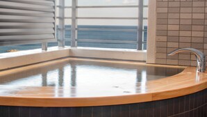 Un baño con una bañera grande, una ventana con vistas al océano y un grifo moderno.