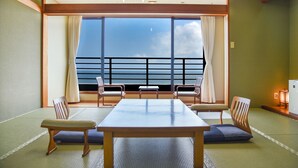 Una habitación con tatamis, una mesita baja y sillas, un ventanal con vistas al mar y una pequeña mesa con una lámpara.