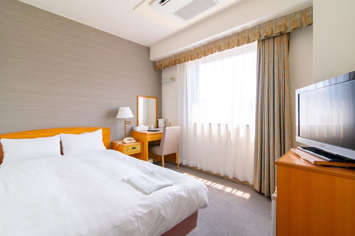 A hotel room with a large bed, a desk with a chair, a television, and a window with curtains.
