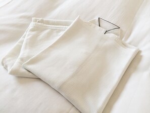 A neatly folded white garment on a bed with a smooth texture. - Bright Park Hotel (Kochi)