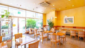 A restaurant with multiple tables and chairs, a vending machine, and a large window with a view of greenery outside. - Bright Park Hotel (Kochi)